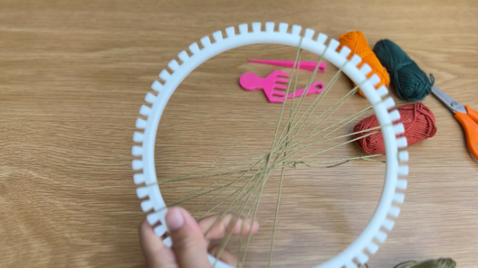 Image of white plastic loom with about half of the pegs looped with green yarn to form the base structure.