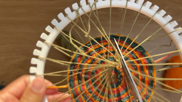 Image of a white plastic loom with a woven structure. Scissors are being used to cut off the backside of the base structure.